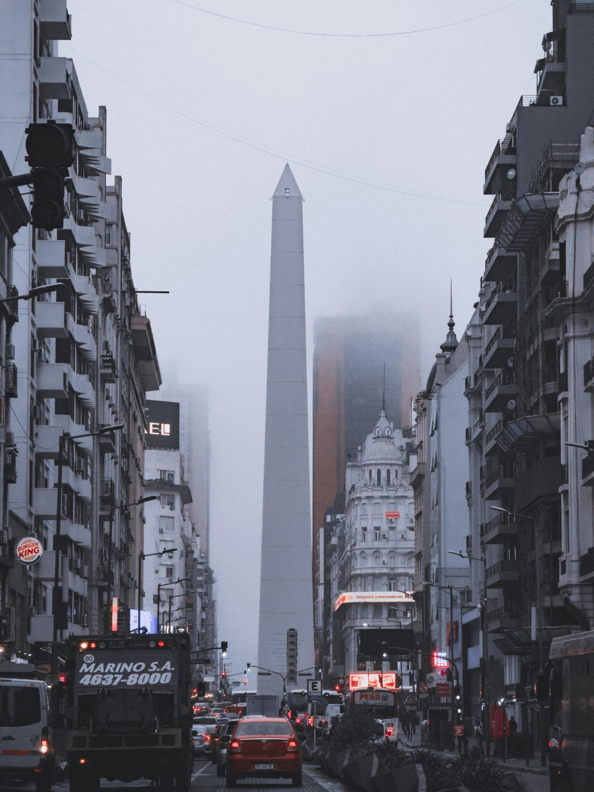 The Obelisco in fog above evening traffic on a Buenos Aires avenue