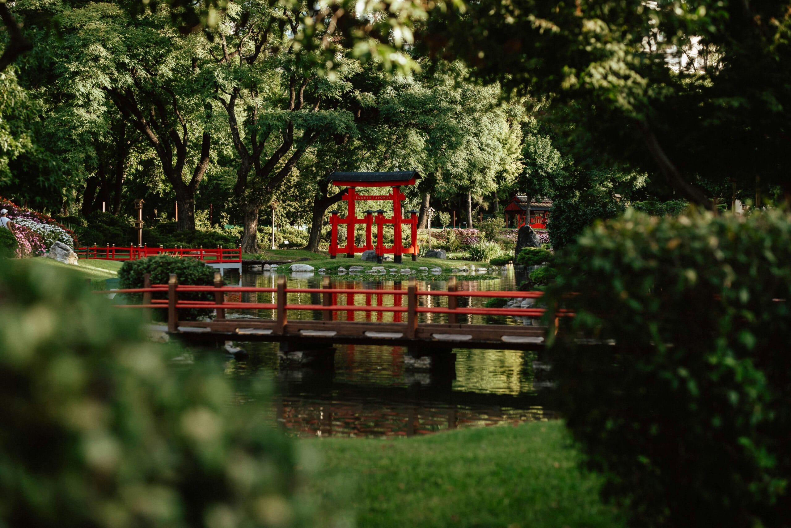 A red torii and two wooden bridges reflected in the pond at the Jardin Japones in Palermo