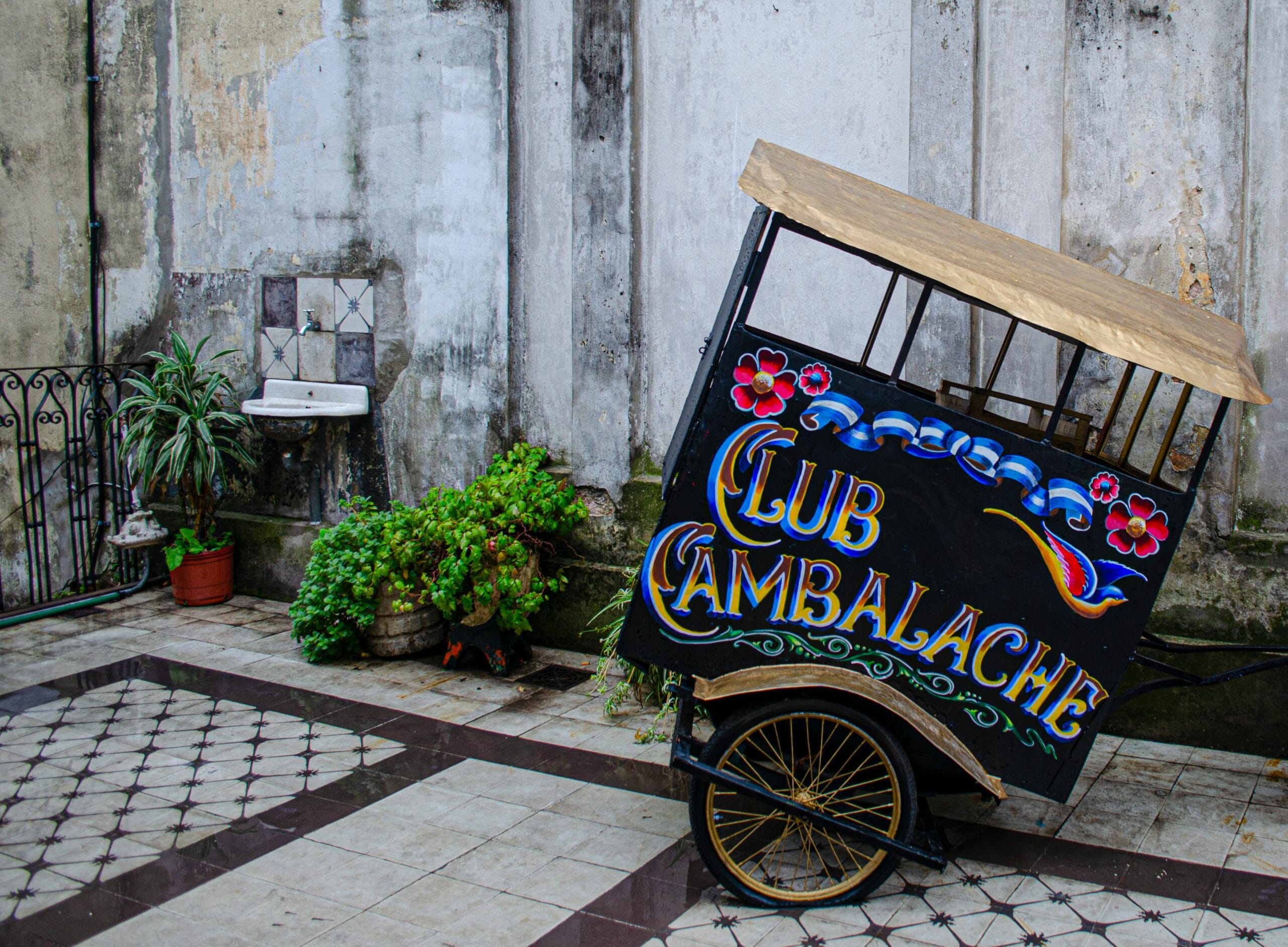 A cart painted in the fileteado style, lettered Club Cambalache, parked in a tiled courtyard