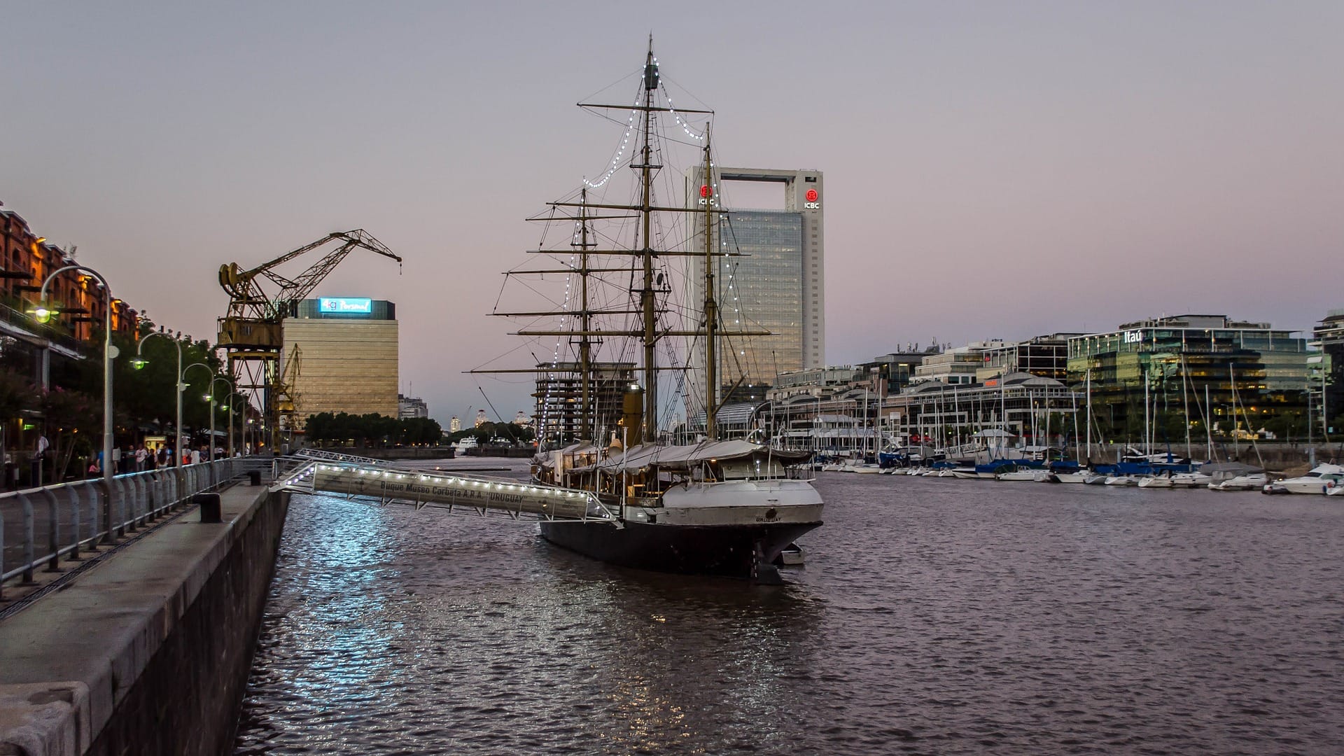 The corvette ARA Uruguay, now a museum ship, moored in Puerto Madero at dusk, with an old harbour crane and the marina behind it