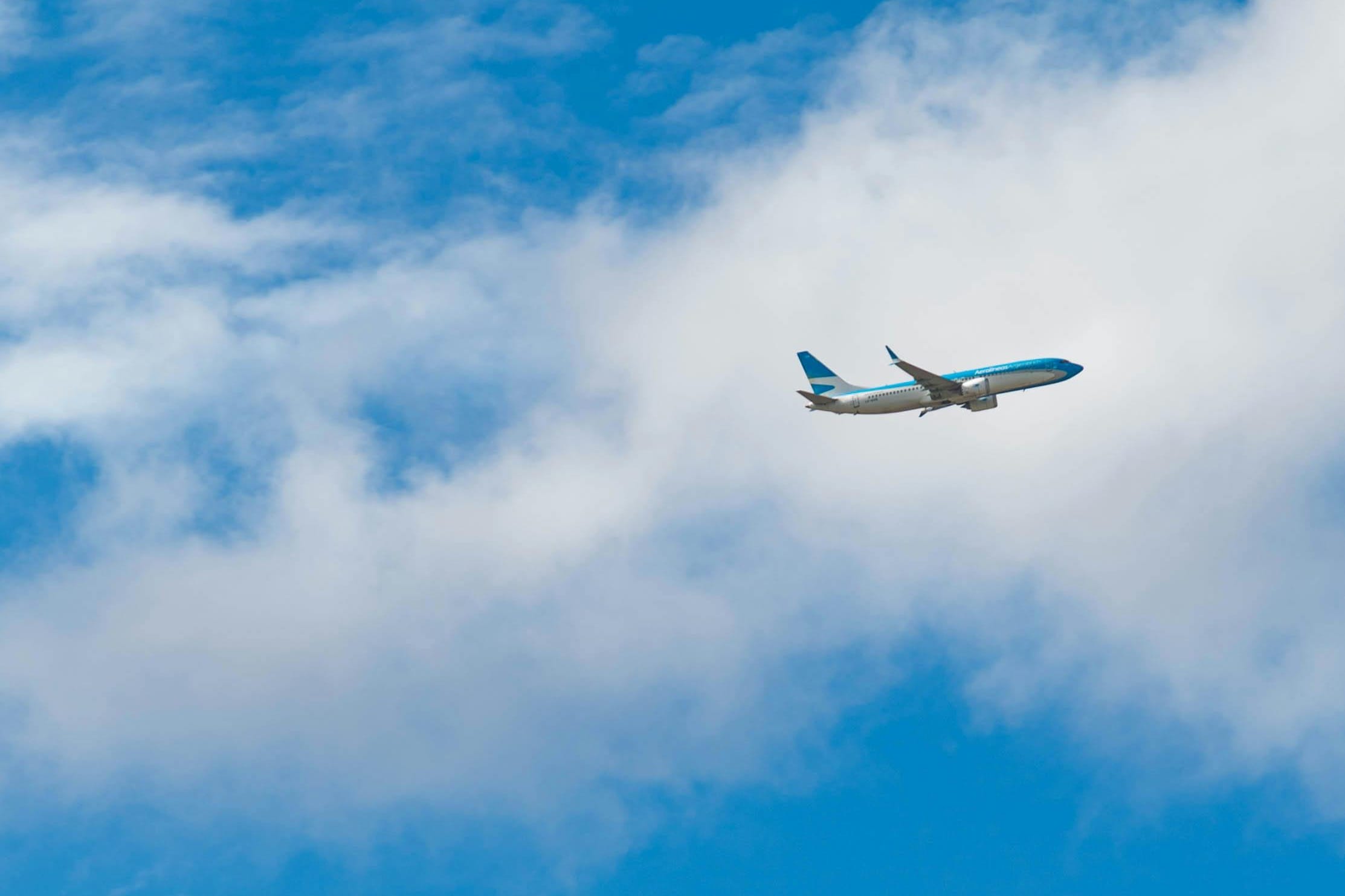 An Aerolíneas Argentinas jet flying through white clouds in a blue sky