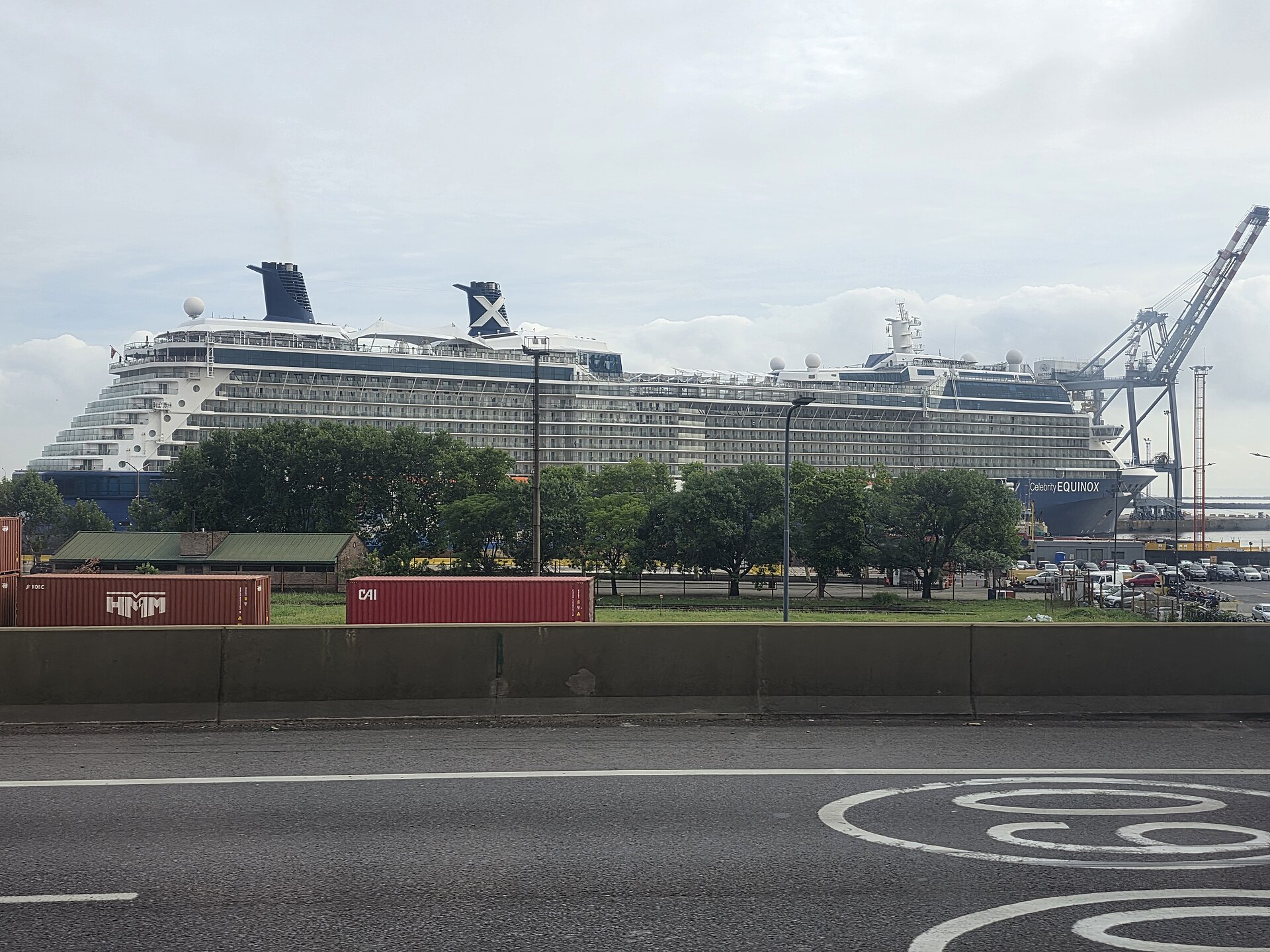 El crucero Celebrity Equinox amarrado en el puerto de Buenos Aires, detrás de contenedores rojos y junto a una grúa de carga, en un día nublado