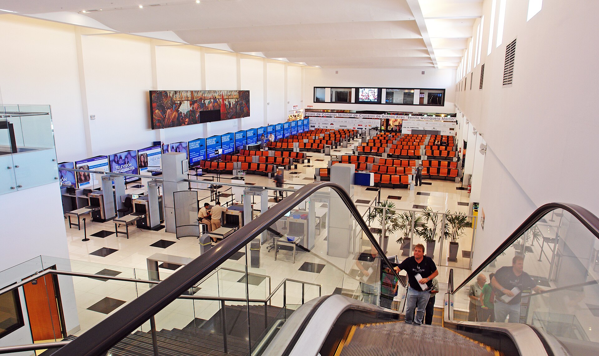 The waiting hall of the Quinquela Martín cruise terminal in Buenos Aires, seen from the escalator: rows of orange seats, the security scanners and a large mural of a port scene